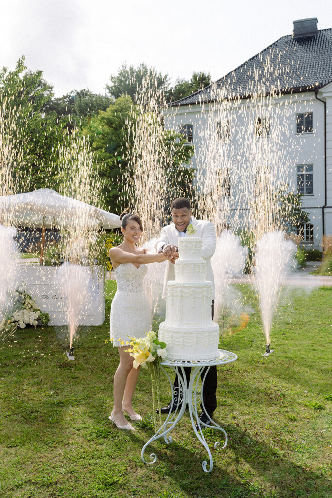 Hochzeitspaar schneidet Torte bei Feuerwerk an.